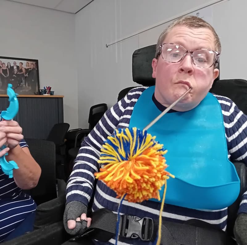 SIL service user holding a colourful woollen pompom she has just made using a mouth tool