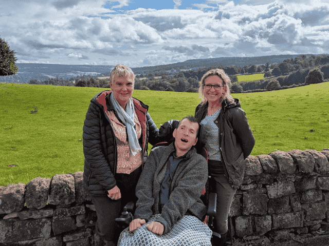 Two Independent Living support workers with man in wheelchair posing against stunning Yorkshire landscape
